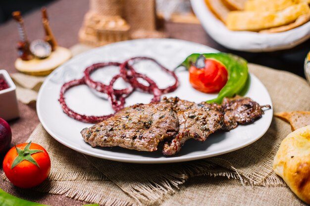 Kebab del basturma della carne di vista frontale con il pomodoro e il peperoncino sulla griglia con la cipolla in sumac