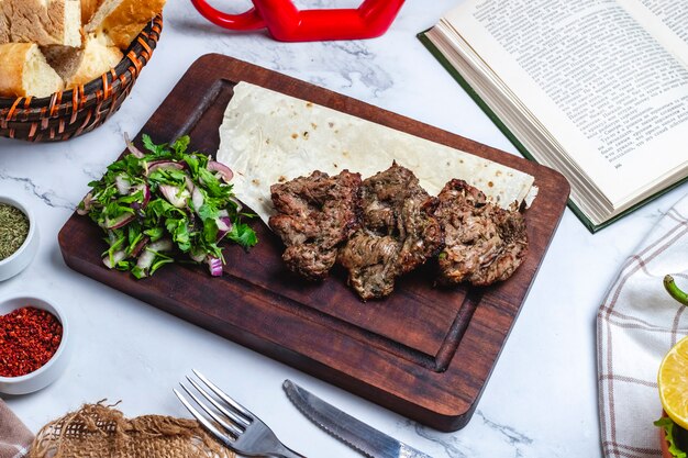 Kebab del basturma della carne di vista laterale sul pane della pita con le erbe e le cipolle su un bordo