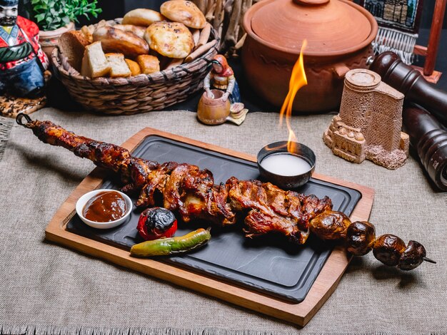 Kebab di carne di vista laterale su uno spiedino con patate alla griglia e verdure con salsa e fuoco su una tavola