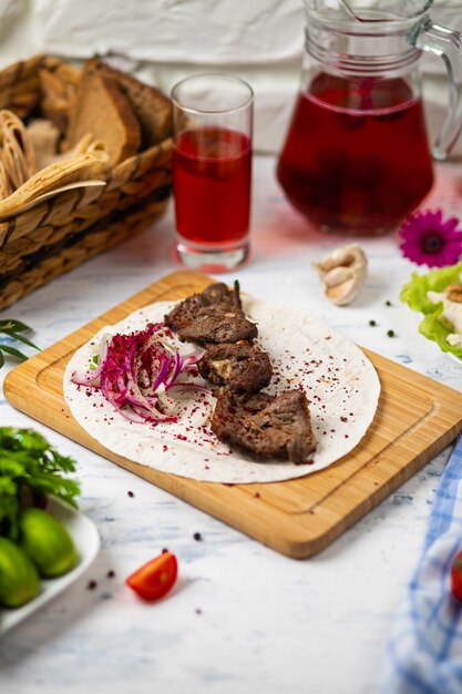 Kebab di manzo con cipolle, sumakh e lavash su un piatto di legno servito con vino e verdure