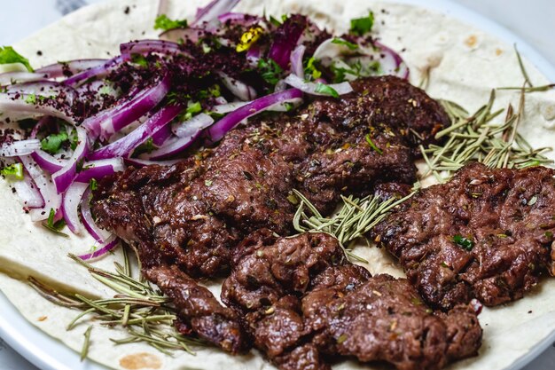 Kebab di vista laterale grigliato di carne di manzo con verdure a cipolla rossa e rosmarino su pita