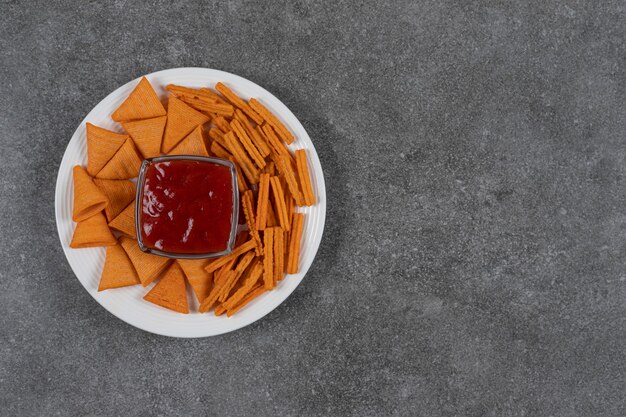 Ketchup, patatine di mais e pane secco sul piatto sulla superficie in marmo