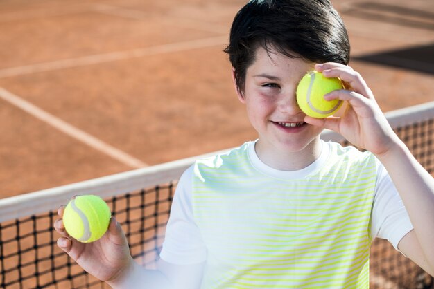 Kid che copre il suo occhio con la pallina da tennis