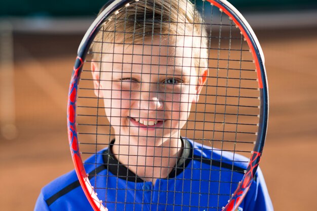 Kid si copre la faccia con una racchetta da tennis