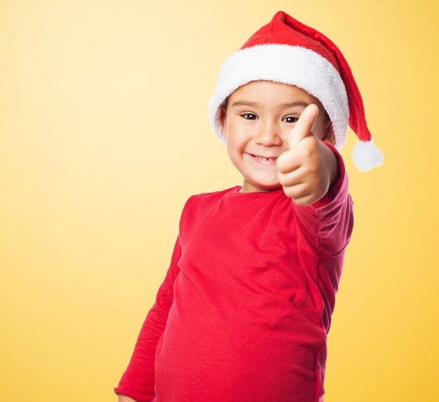 Kid sorridente con il pollice alto ed il cappello di Babbo Natale