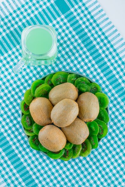 Kiwi fresco con kiwi essiccato, bevanda in un piatto sul panno da picnic e sfondo bianco, vista dall'alto.