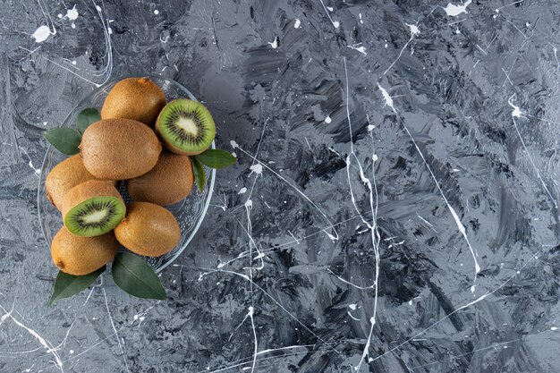 Kiwi interi e affettati con foglie poste in una tavola di vetro.