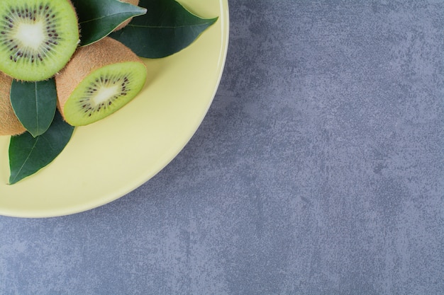 Kiwi interi e mezzo sul piatto sulla tavola di marmo.