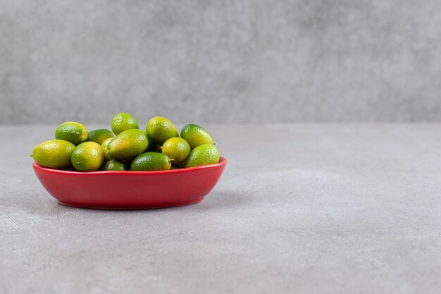 Kumquat in una ciotola ovale rossa su fondo marmo.