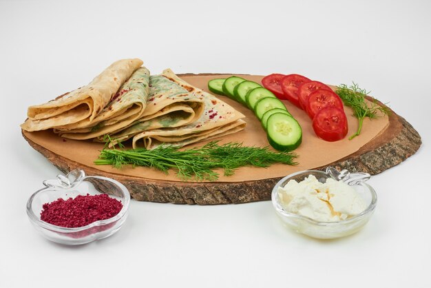 Kutab caucasico con spezie e verdure su una tavola di legno sul bianco.
