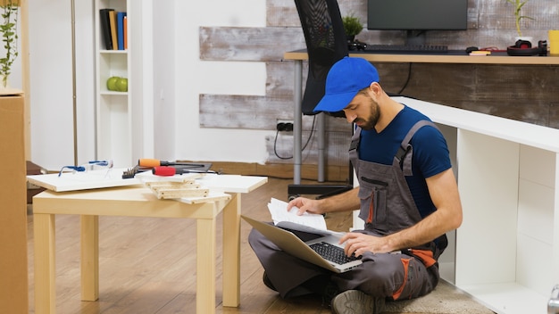L'addetto all'assemblaggio di mobili utilizza il laptop per consultare le istruzioni. Tuttofare che fa un buon lavoro.