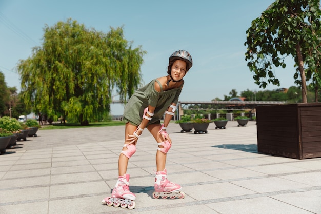 L'adolescente in un casco impara a cavalcare sui pattini a rotelle tenendo un equilibrio o sui rollerblade e girare per le strade della città nella soleggiata giornata estiva. Stile di vita sano, infanzia, hobby, attività per il tempo libero.