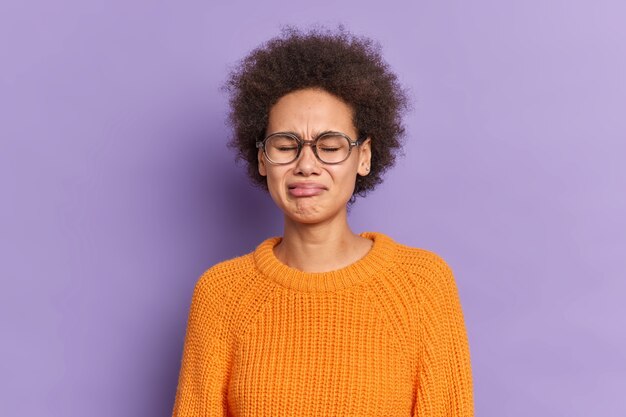 L'adolescente infelice triste con i capelli ricci si sente frustrato e deluso indossa un maglione lavorato a maglia arancione con occhiali trasparenti.