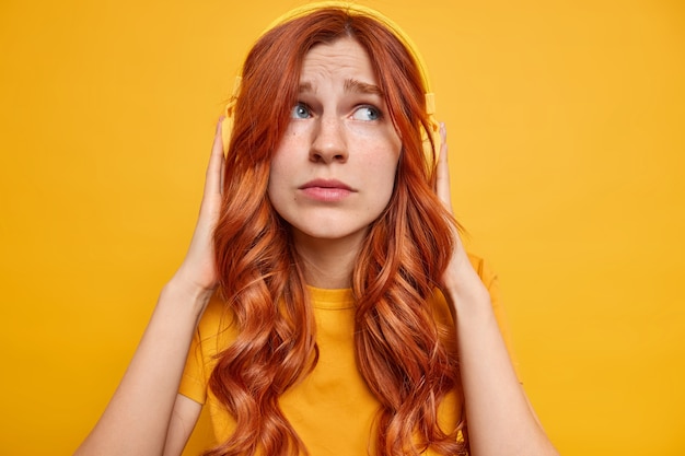 L'adolescente malinconico allo zenzero dispiaciuto tiene le mani sulle cuffie stereo pensa a qualcosa di triste mentre ascolta musica vestita casualmente guarda da parte tristemente