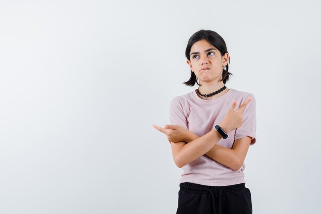 L'adolescente pensante sta puntando lateralmente con le mani incrociate su sfondo bianco