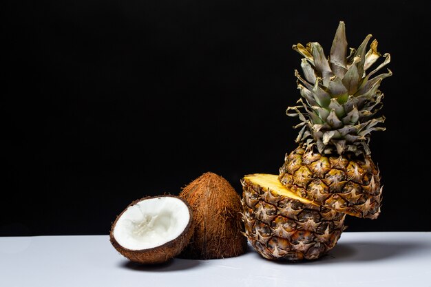 L'ananas e la noce di cocco hanno tagliato a metà su una tabella sul nero