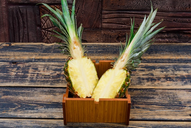 L'ananas ha tagliato a metà in un piatto di legno su vecchio legno e sulle mattonelle di pietra scure, vista laterale.