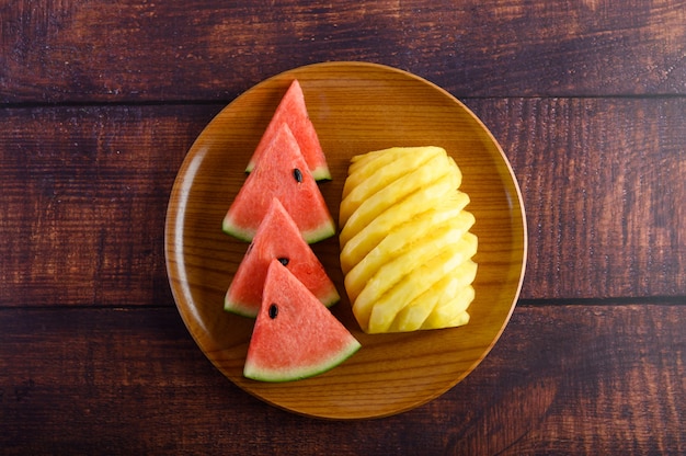 L'anguria e l'ananas hanno tagliato a pezzi su un piatto di legno