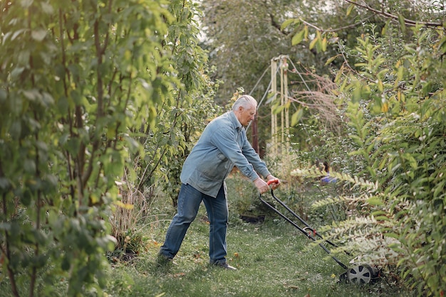 L'anziano falcia l'erba nel cortile con un tosaerba