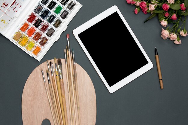 L'area di lavoro dell'artista con laptop, vernici, pennelli, fiori sul nero