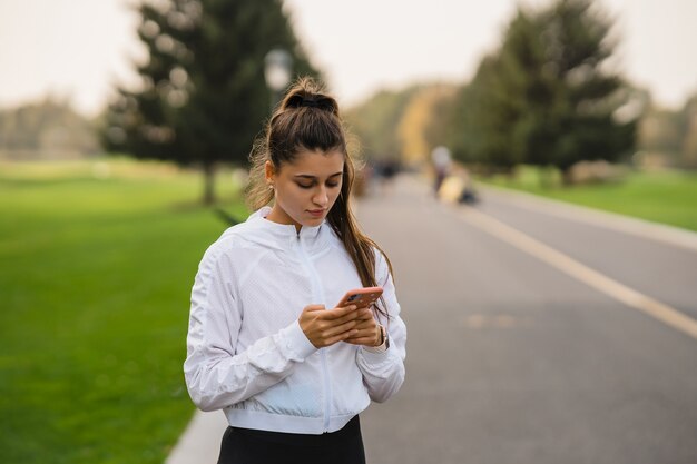 L'atleta della giovane donna tiene e utilizza lo smartphone dopo il jogging