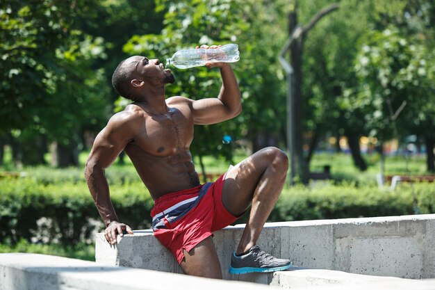 L'atleta in forma che riposa e beve acqua dopo gli esercizi allo stadio