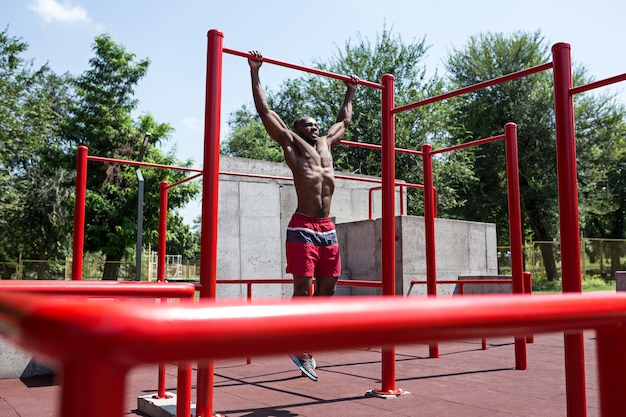 L'atleta in forma facendo esercizi allo stadio. Uomo afro o afroamericano all'aperto in città. Tirare su esercizi sportivi. fitness, salute, concetto di stile di vita