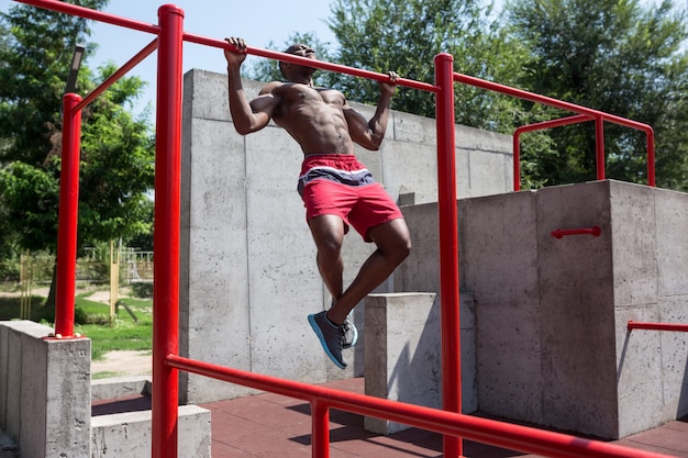 L'atleta in forma facendo esercizi allo stadio. Uomo afro o afroamericano all'aperto in città. Tirare su esercizi sportivi. fitness, salute, concetto di stile di vita