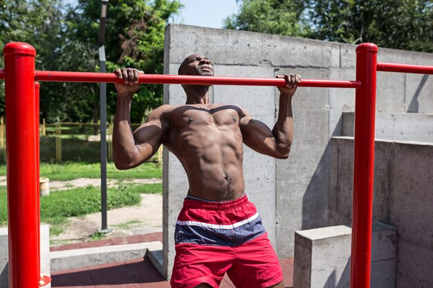 L'atleta in forma facendo esercizi allo stadio. Uomo afro o afroamericano all'aperto in città. Tirare su esercizi sportivi. fitness, salute, concetto di stile di vita