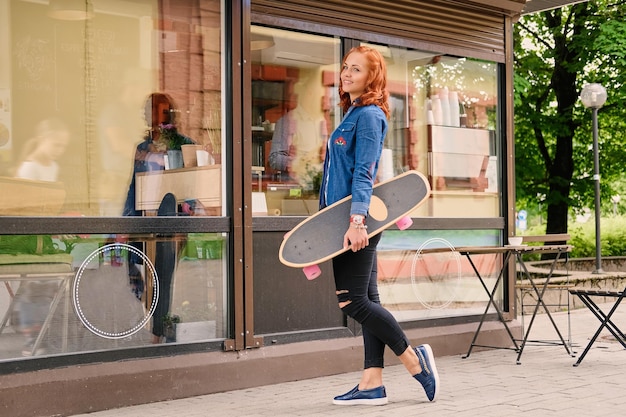 L'attraente donna dai capelli rossi tiene Longboard nel parco cittadino.