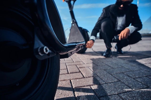 L'elegante uomo barbuto sta caricando il suo scooter elettrico con il caricabatterie in un parcheggio speciale.