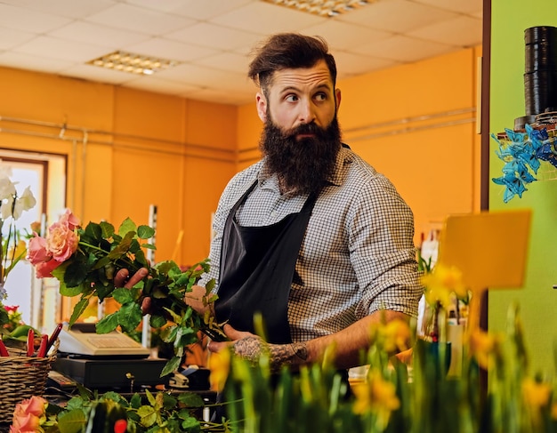 L'elegante venditore di fiori barbuto tiene rose rosa in un negozio di mercato.