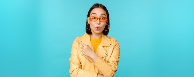 L'immagine della donna asiatica sembra incuriosita pone domande sull'oggetto o sul negozio punta il dito a sinistra con l'espressione del viso sorpresa si trova su sfondo blu