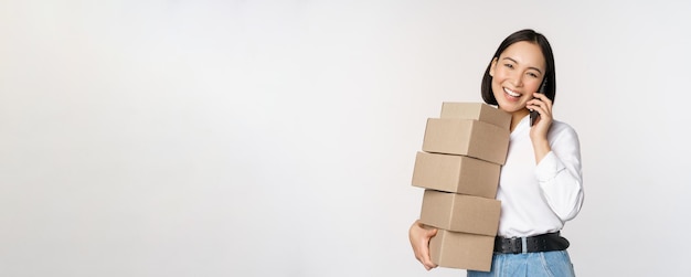 L'immagine della giovane donna d'affari asiatica risponde alla telefonata mentre trasporta le scatole per la consegna in posa su uno sfondo bianco