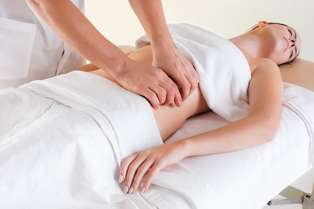 L'immagine di bella donna nel salone di massaggio e le mani maschii sul suo corpo
