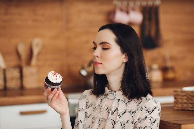 L'immagine di una bella donna caucasica con i capelli corti e scuri in un maglione accogliente tiene un marshmallow e sorride