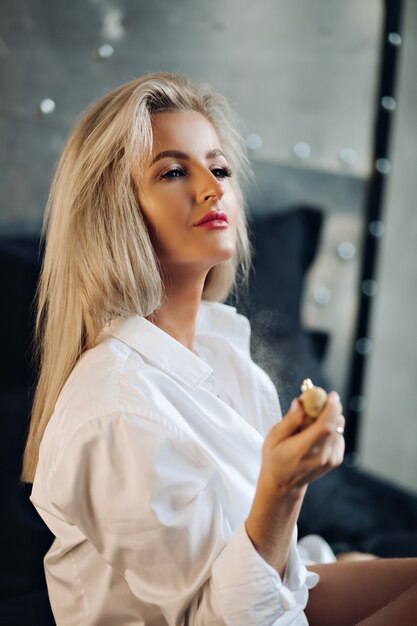 L'immagine di una bellissima giovane donna caucasica con lunghi capelli biondi in camicia da uomo posa per la telecamera in cucina