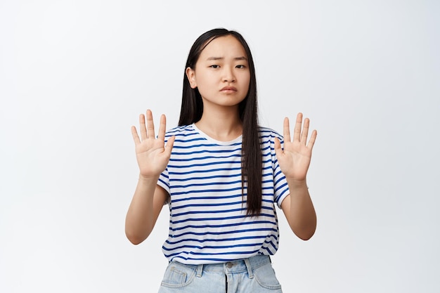 L'immagine di una donna asiatica seria dice di smettere di dire di non rifiutare qualcosa che mostra un gesto di rifiuto vietare l'azione sfondo bianco