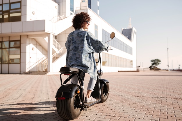 L'immagine integrale di vista posteriore della giovane donna guida sulla motocicletta