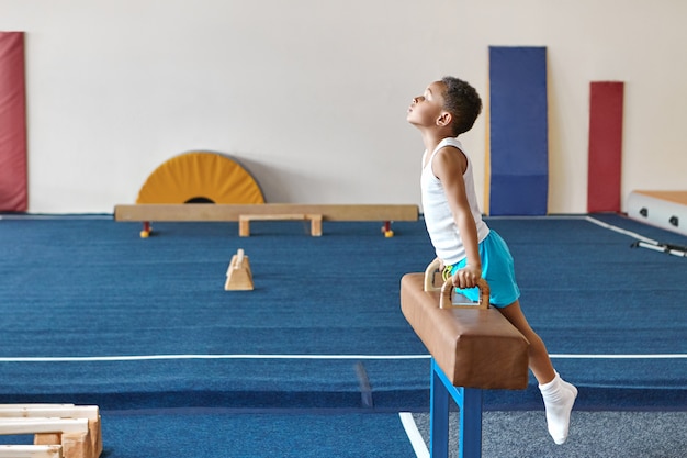 L'immagine orizzontale del ginnasta afroamericano esperto del ragazzo che prepara per la concorrenza di ginnastica artistica