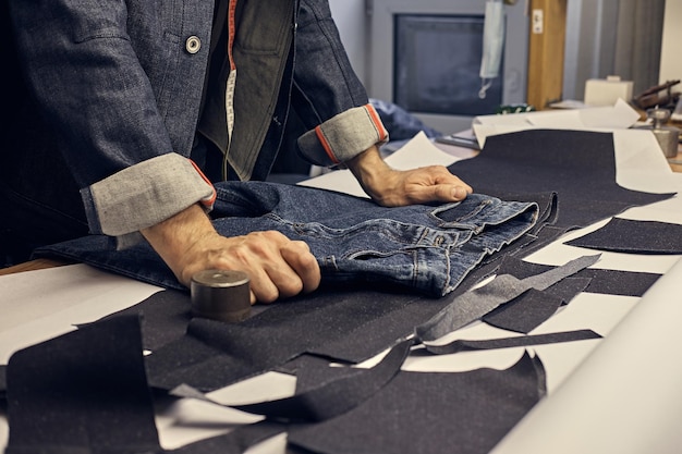 L'immagine ritagliata del sarto effettua le misurazioni dei jeans con un metro al laboratorio di cucito.