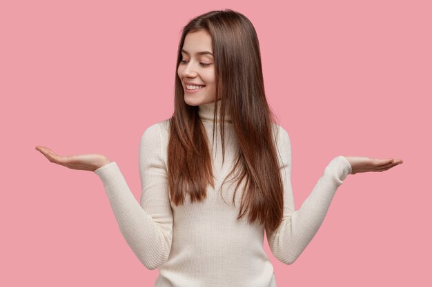 L'individuo felice alza due palmi, sente esitazione tra due oggetti, ha un'espressione del viso soddisfatta, vestito con un maglione bianco caldo