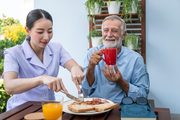 L'infermiera assiste l'anziano anziano a fare colazione e bere caffè con la tazza in mano nella casa di cura