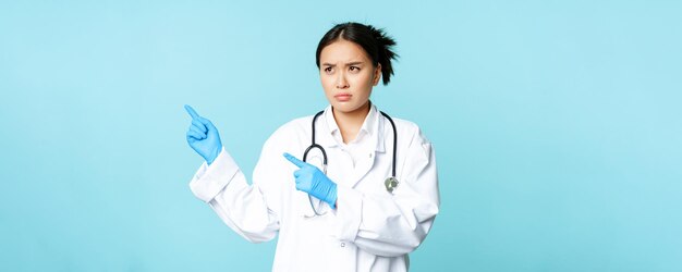 L'infermiera o il medico asiatico arrabbiato del lavoratore esprimono la disapprovazione che indica a sinistra e le sopracciglia del solco stanno