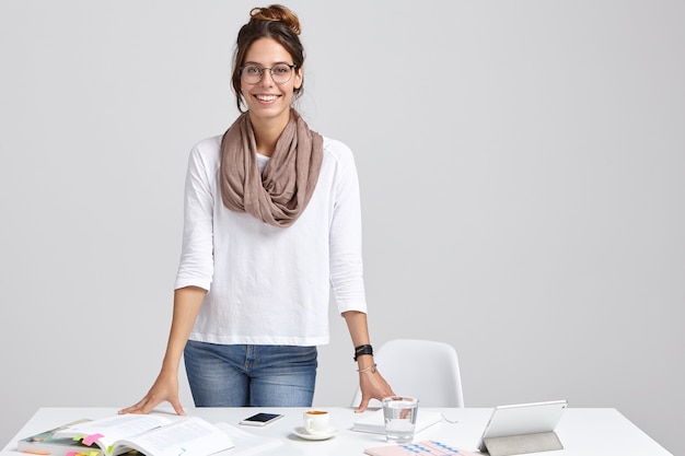 L'insegnante femminile intelligente soddisfatto indossa jeans e maglione bianco