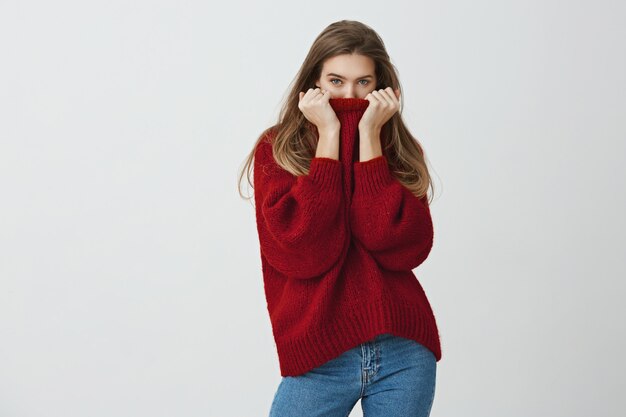 L'inverno è vicino. Bella donna snella in maglione sciolto alla moda che nasconde il viso nel colletto mentre guarda, sente freddo o arrossisce di complimenti, in piedi.