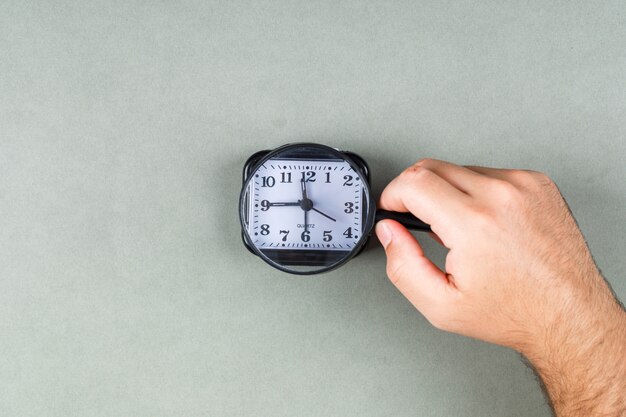 L'orologio sta ticchettando e concetto della gestione di tempo con l'orologio sulla vista superiore del fondo grigio. mani che tengono una lente d'ingrandimento. immagine orizzontale