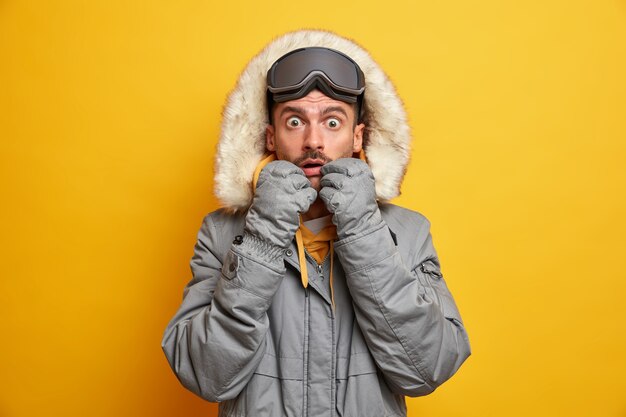 L'uomo adulto caucasico sbalordito fissa gli occhi spalancati indossa vestiti caldi per gli occhiali da sci della stagione fredda gode dell'hobby preferito e ha riposo attivo.
