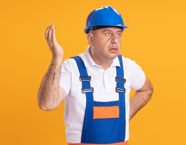 L'uomo adulto caucasico senza tracce del costruttore in uniforme sta con la mano alzata e guarda a lato sull'arancia