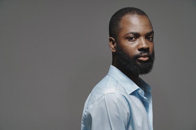 L'uomo africano in uno studio. Muro bianco. Uomo in una camicia blu.